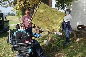 Pilgergruppe mit Frau im Rollstuhl mit Pilgerfahne